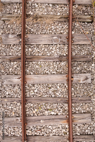 Top view of the old rusty rails with cracked wooden sleepers with a mound of small stones. Old vintage railway tracks