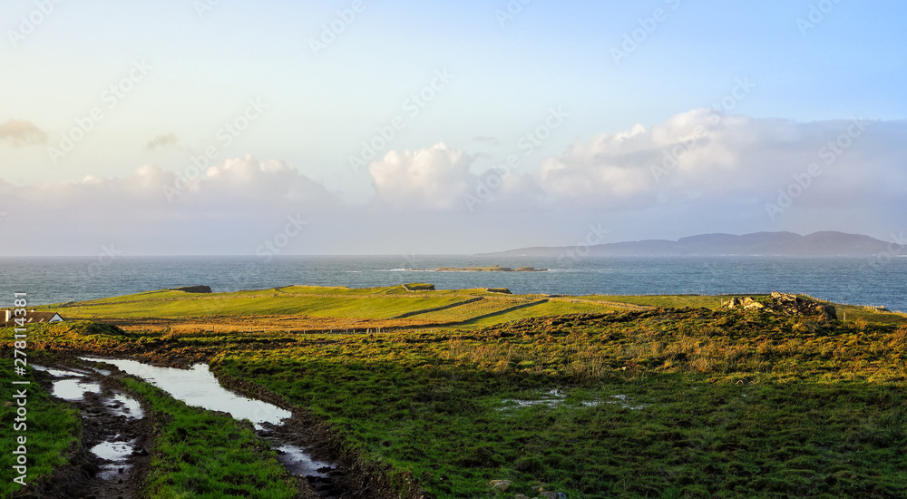 Dirt road and green fields on the coast, with islands and mountains in a distance, Wiled Atlantic Way