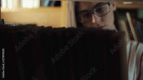 Attractive young woman looking for a book from a bookshelf in library