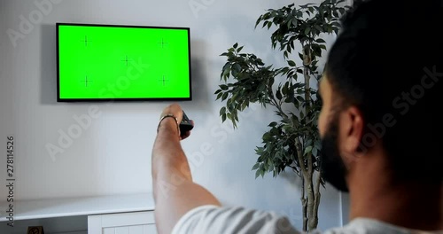 African-american male turning on greenscreen tv with remote control, advertisement template, backview