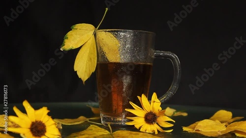 A transparent glass cup is wet in the rain of hot tea in the midst of an autumn landscape: yellowed fallen leaves, yellow flowers. autumn mood.