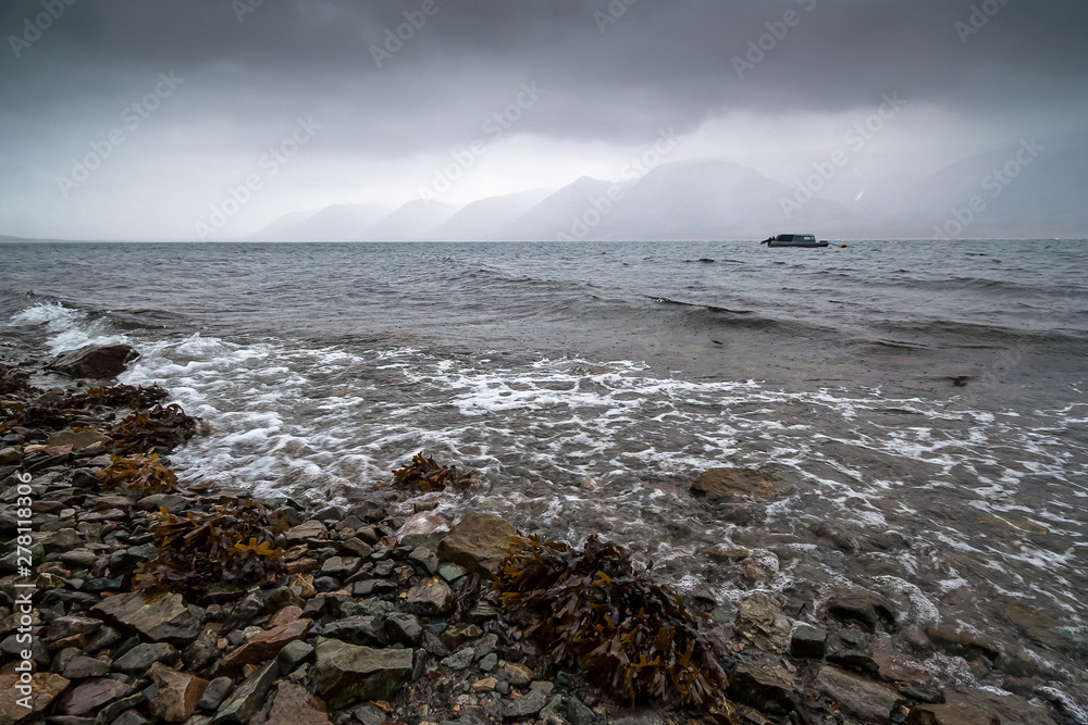 Obraz premium Sea bay in the rain. Severe seascape with coast and mountains. Boat in the sea. Surf and seaweed. Autumn weather. Arctic nature. Egvekinot Bay, Kresta Gulf, Bering Sea, Chukotka, Far East of Russia.