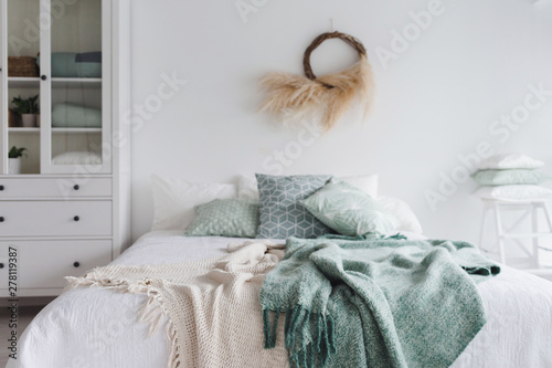 Modern scandinavian sunny bedroom with plants , floral pattern bedding and pilows. Space with white walls and eco decor. A bed with a mint plaid.