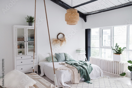 Modern scandinavian sunny bedroom with plants , floral pattern bedding and pillows. Space with white walls and wide window. Eco decor. Real photo.