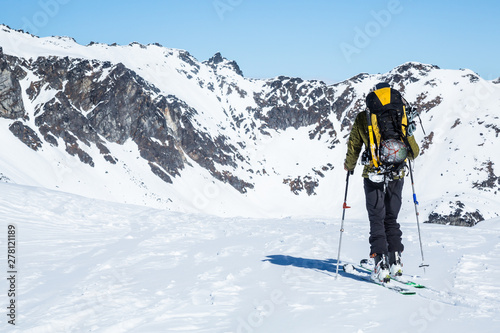 Skier standing on a hill overlooking large cliffs and couloirs above hte Snowbird Glacier of the Alaska backcountry.