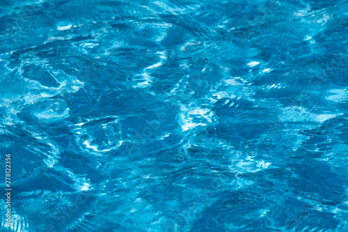 Blue and bright ripple water surface in swimming pool with sun reflection.