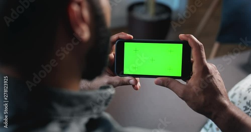 Male sitting indoors and holding prekeyed smartphone horizontally, template for advertisement