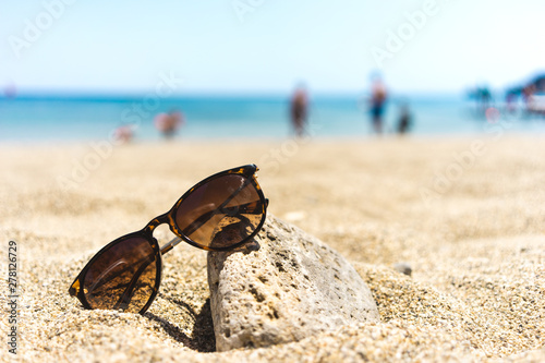 Brown sunglasses leaned towards a stone on a beach