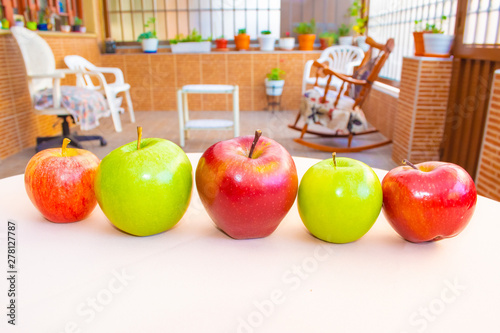 Green and red apples intercalated in a row with a beautiful garden in the background photo