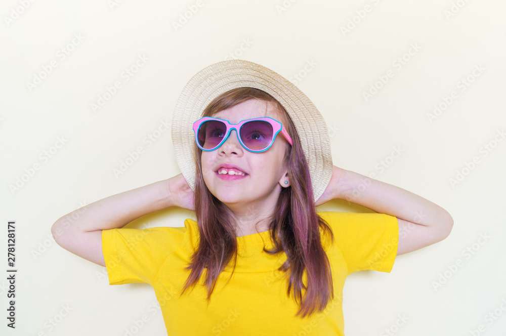 The child sits in the room on the floor emotion on his face. Little girl in a yellow T-shirt, glasses and a straw hat. The child sits in the room on the floor emotion on his face. Little girl in a yellow T-shirt, glasses and a straw hat.