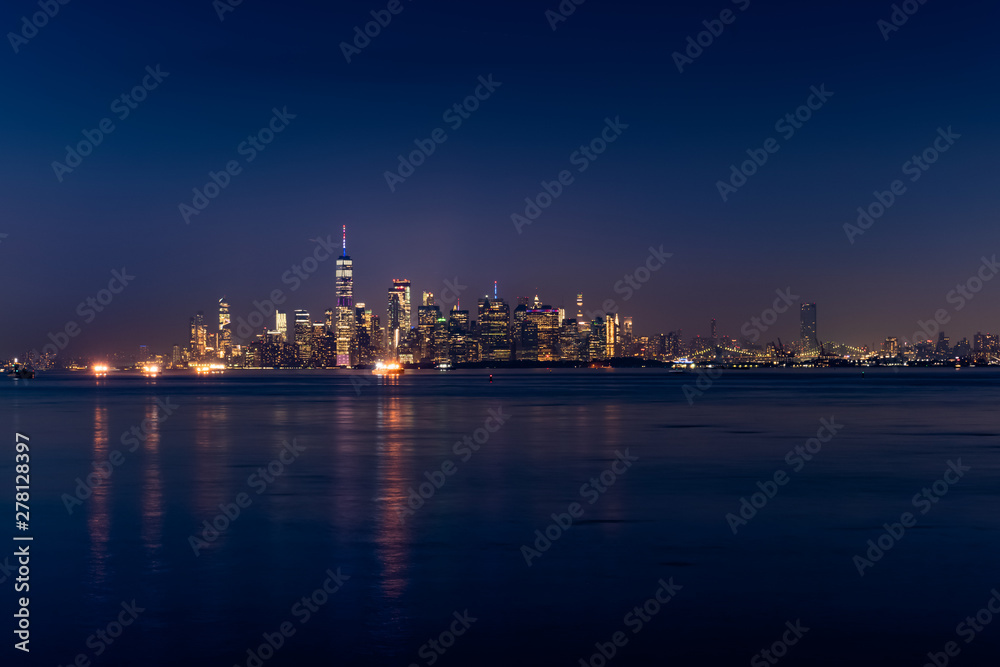 New York City Manhattan skyline illuminated with lights at dusk after sunset, view from New York Bay and Staten Island, water view