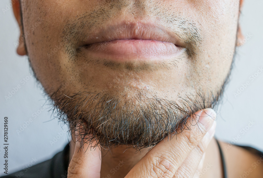 Cropped shot of Asian man touching his beard grows on a part of lower face.  Beard