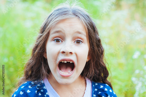 Little adorable girl screaming in the field in nature, daylight, summer