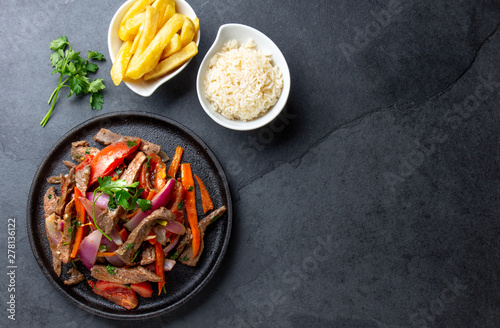 Peruvian dish Lomo saltado - beef tenderloin with purple onion, yellow chili, tomatoes served onvblack plate with french fries and rice. Top view photo