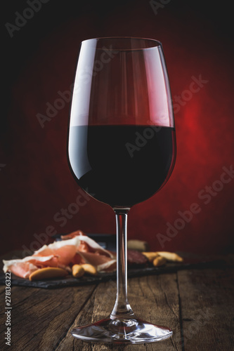 Glass of red wine with ham serrano on wooden background