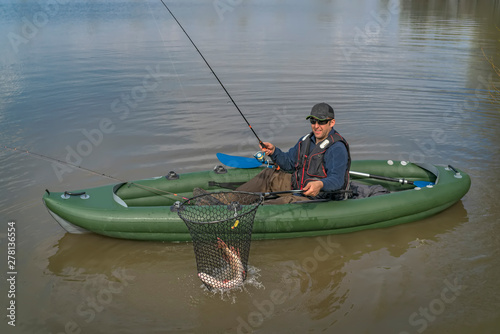 Kayak fishing. Fisherman caught pike fish on inflatable boat with fishing tackle at lake.