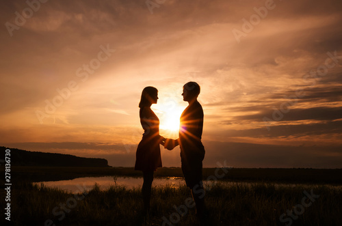 A pair - silhouettes of a man and a woman - are standing against the background of the setting sun with beautiful rays. Romantic concept for Valentine's Day, declaration of love, a family. Copy space.