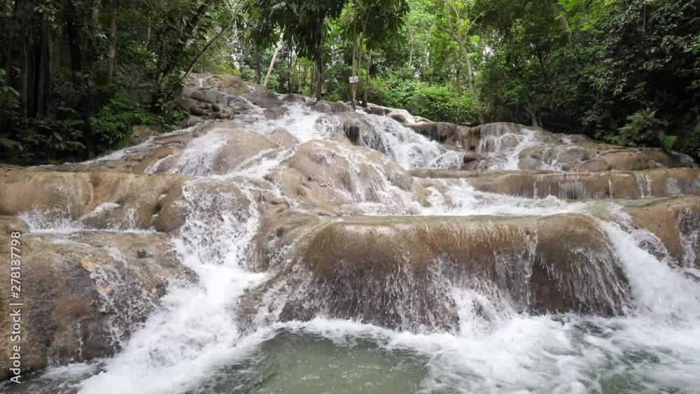 A beautiful view of water cascading over rocks in Dunn's River Falls waterfall with lush vegetation in background beyond in Ocho Rios on the tropical island of Jamaica a popular travel destination A beautiful view of water cascading over rocks in Dunn's River Falls waterfall with lush vegetation in background beyond in Ocho Rios on the tropical island of Jamaica a popular travel destination