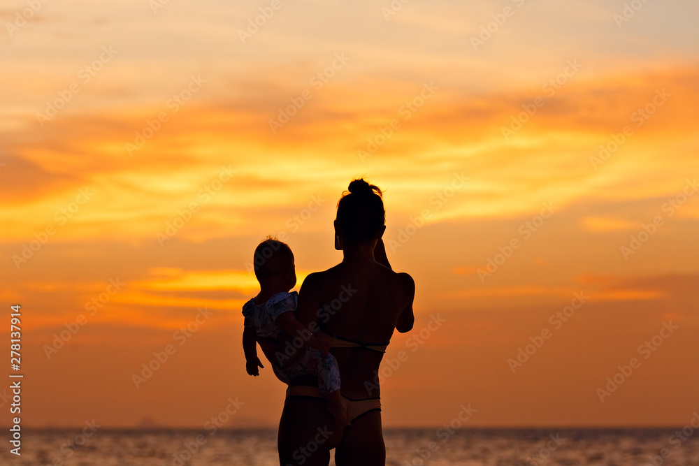 Silhouette of mother with her toddler against the sunset and lens flare