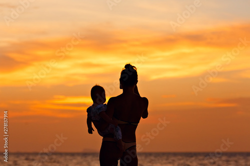 Silhouette of mother with her toddler against the sunset and lens flare