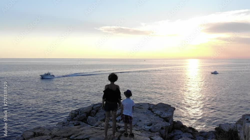 Mother and her child watching boats on water and beautiful sunset on the seashore Mother and her child watching boats on water and beautiful sunset on the seashore