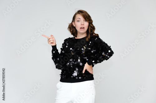 Portrait below the belt on a white background pretty young brunette woman in a black sweater and white trousers with glitters. Standing in different poses, talking, showing emotions.