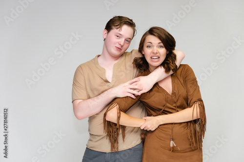 Portrait below the belt on a white background pretty young brunette woman in a brown dress and a young man in a brown shirt. Standing in different poses, talking, showing emotions.