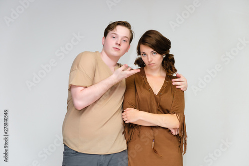 Portrait below the belt on a white background pretty young brunette woman in a brown dress and a young man in a brown shirt. Standing in different poses, talking, showing emotions.