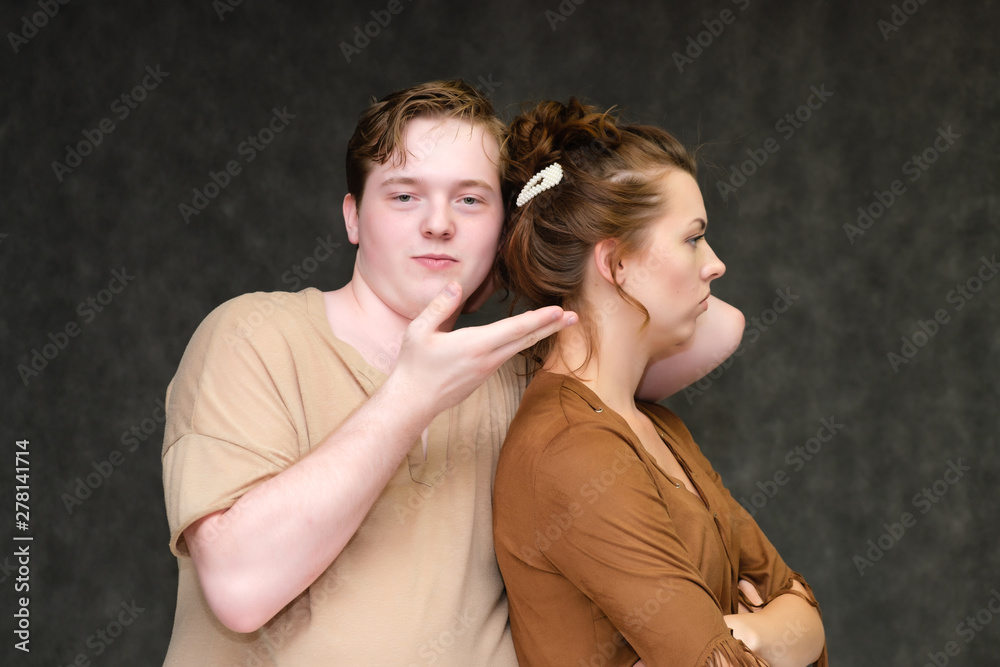 A portrait below the belt on a gray background of a pretty young brunette woman in a brown dress and a young man in a brown shirt. They stand in different poses, talking, showing emotions.