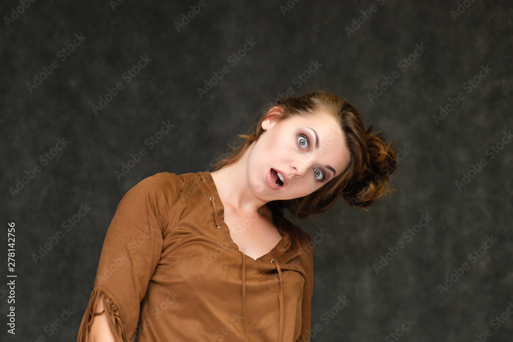 Portrait below breast over gray background of pretty young brunette woman in brown dress with beautiful hair. Standing in different poses, talking, showing with hands, demonstrating emotions.