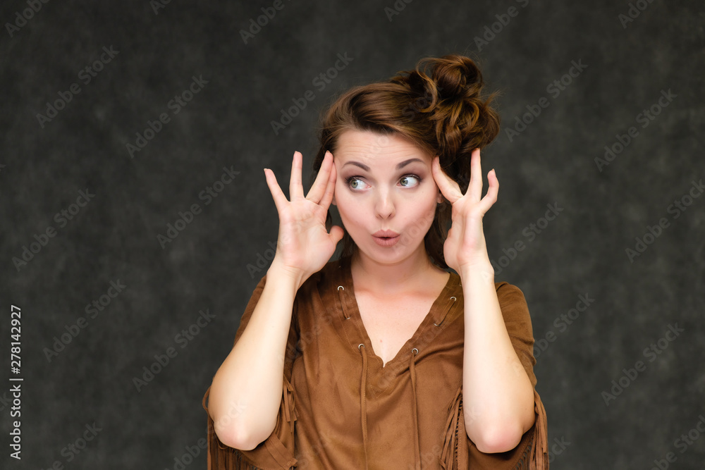 Portrait below breast over gray background of pretty young brunette woman in brown dress with beautiful hair. Standing in different poses, talking, showing with hands, demonstrating emotions.