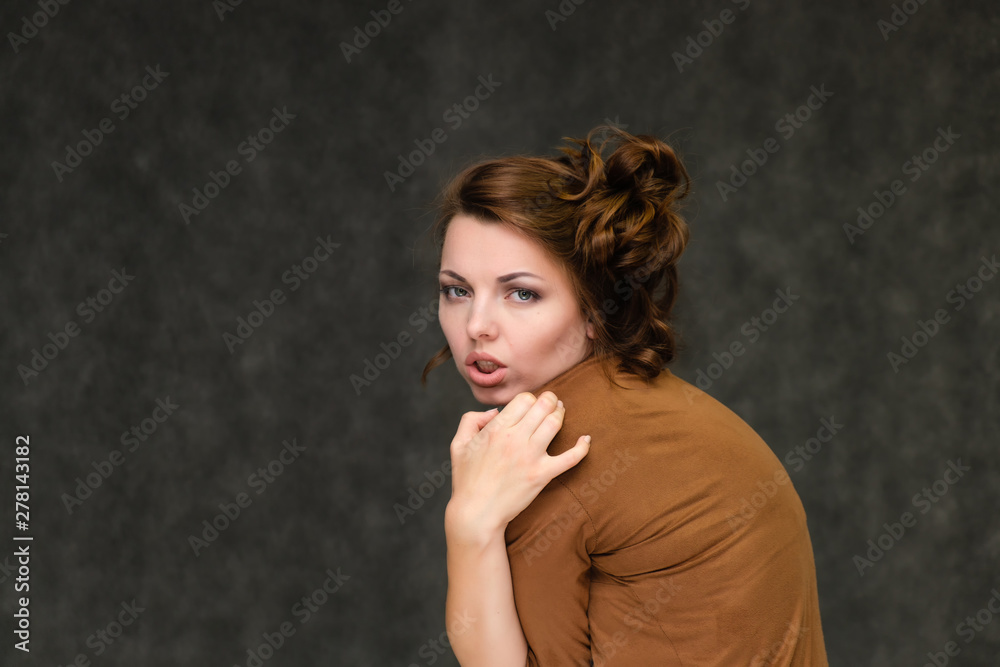 Portrait below breast over gray background of pretty young brunette woman in brown dress with beautiful hair. Standing in different poses, talking, showing with hands, demonstrating emotions. Portrait below breast over gray background of pretty young brunette woman in brown dress with beautiful hair. Standing in different poses, talking, showing with hands, demonstrating emotions.