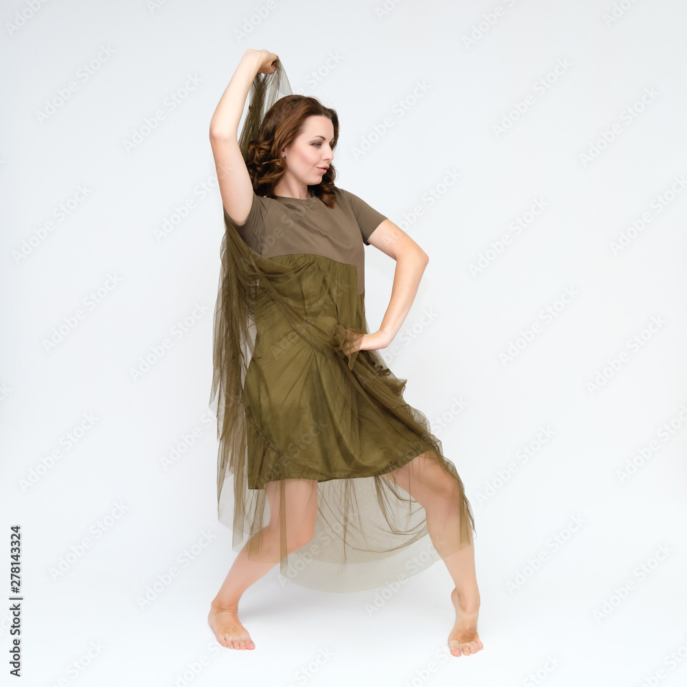 Naklejka premium Portrait in full growth on a white background pretty young brunette woman in a green dress with beautiful hair. Standing in different poses, talking, showing hands, demonstrating emotions.