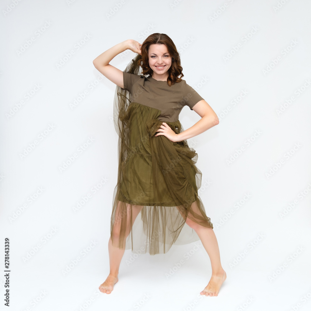 Naklejka premium Portrait in full growth on a white background pretty young brunette woman in a green dress with beautiful hair. Standing in different poses, talking, showing hands, demonstrating emotions.