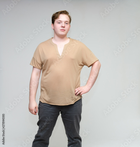 Portrait of a knee on a white background cute young man in a brown T-shirt in jeans. Standing right in front of the camera in various poses, talking, demonstrating emotions. © Вячеслав Чичаев