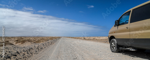 Fototapeta Naklejka Na Ścianę i Meble -  Landscape of a typical white dirt road near El Coralejo Fuerteventura Canary Island Spain. 4x4 van along an offroad path, blue sky with clouds in background. Travel adventure and freedom concept.