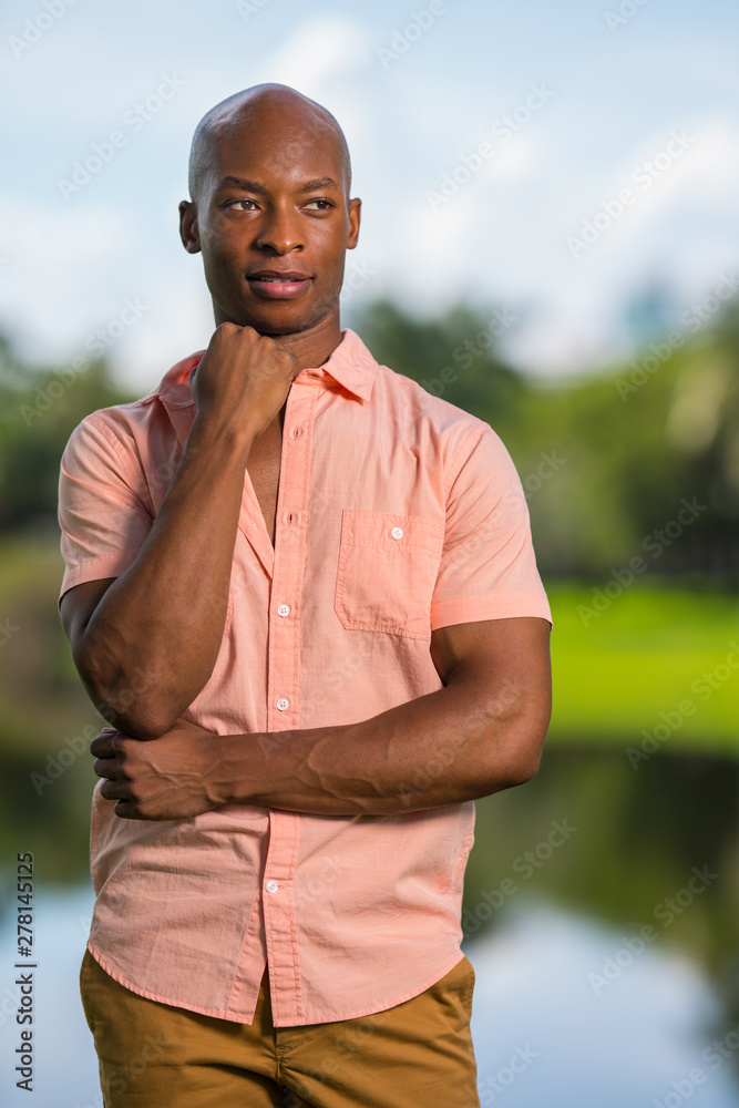 Photo of a handsome young black man smiling and looking of camera. Hand posed under his chin in an outdoor setting