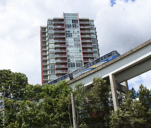 Vancouver SkyTrain in New Westminster BC Canada on tracks going past apartment building on bright cloudy day