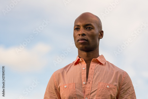Portrait of a handsome black businessman glancing over the camera. Light blue cloudy sky in the background with copyspace