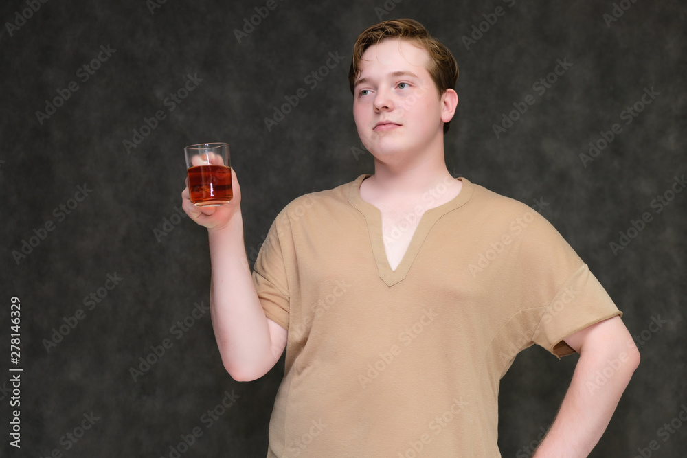 Portrait to the waist on a gray background of a handsome young man in a brown T-shirt with a mug of tea in his hands. standing in different poses, talking, demonstrating emotions. Portrait to the waist on a gray background of a handsome young man in a brown T-shirt with a mug of tea in his hands. standing in different poses, talking, demonstrating emotions.