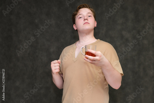 Portrait to the waist on a gray background of a handsome young man in a brown T-shirt with a mug of tea in his hands. standing in different poses, talking, demonstrating emotions.