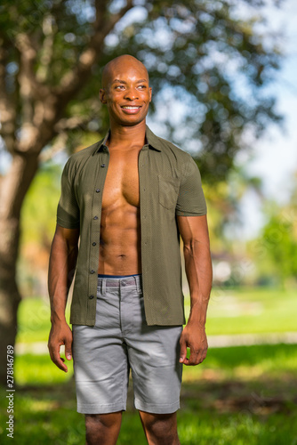 Sexy male model posing in the park with shirt unbuttoned showing muscular chest