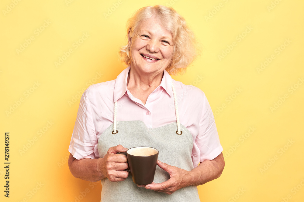 old cheerful positive woman holding coffee cup on yellow background ,barista concept. lifestyle, free time, spare time. close up portrait old cheerful positive woman holding coffee cup on yellow background ,barista concept. lifestyle, free time, spare time. close up portrait