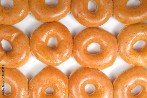 Top view flat lay close up of plain glazed donuts in a white box isolated. One dozen donuts. The original glazed donut has remained peoples favorite throughout history.