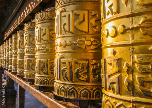 A prayer wheels on a spindle made from metal and wood. Mantra Om Mani Padme Hum is written in Newari language of Nepal on the outside of the wheels. Golden Temple (Kwa Bahal) buddhist temple in Patan photo