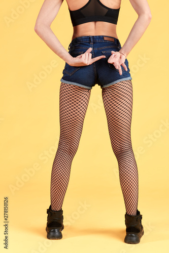 slim sexy girl standing back to the camera making sex gesture with palms. isolated yellow background. studio shot. close up cropped photo