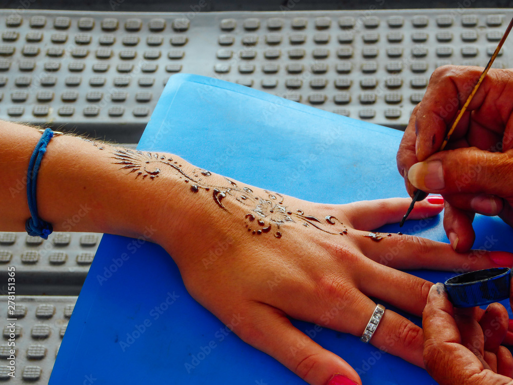 A henna tattoo during the making process. A man is painting the pattern  with a straw.