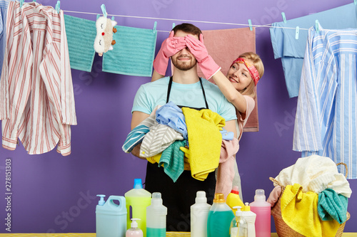 man's eyes are being closed by his girlfriend. close up portrait. woman wants to show her husband effecting washing soap. clean clothes hanging on the clothesline in the background of the photo