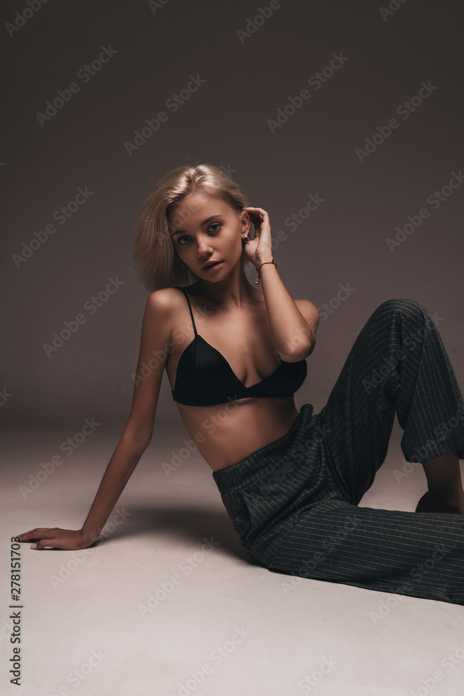 Sexy blonde girl with glamour hairstyle posing on black background in  lingerie and classic trousers. Portrait of stylish seductive hot sexy girl  underwear in the room on gray wall Stock Photo