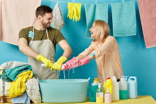 playful bearded man and blonde woman get pleasure from doing laundry. close up photo. isolated blue background. housekeeping photo